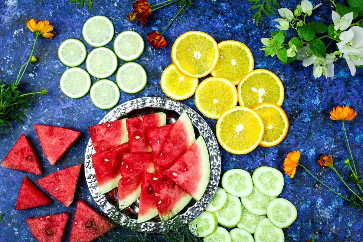 fruits and vegetables including watermelon, oranges, cucumber, and limes on blue table